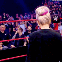 a woman in a black jacket is standing in a wrestling ring with a crowd behind her