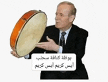 a man in a suit and tie is holding a drum with arabic writing on it .