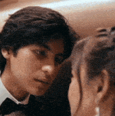 a man in a tuxedo is looking at a woman in a white shirt