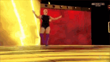 a woman in a black leotard and purple boots is walking on a stage