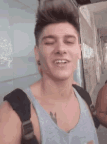 a young man with a tattoo on his chest is smiling and wearing a backpack .
