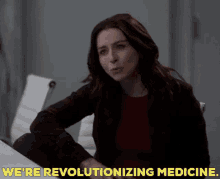 a woman sitting at a table with the words we 're revolutionizing medicine behind her