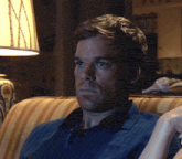 a man in a blue shirt sits on a couch