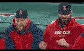 a couple of men wearing red sox shirts are standing next to each other in a stadium .