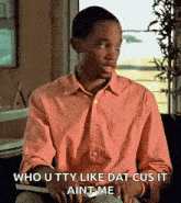 a man in a pink shirt is sitting at a desk and says who utty like dat cus it aint me