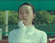 a woman in a white jacket is sitting on a bench with her hand to her mouth