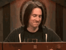 a man with long hair is sitting in front of a table with his hands outstretched .