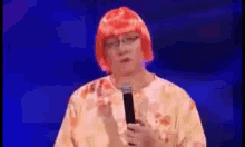 a man wearing a red wig and glasses is holding a microphone in front of a blue background .