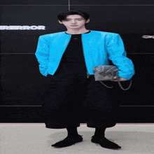 a man wearing a blue jacket and black pants stands in front of a wall that says error