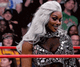 a woman with long white hair is standing in a wrestling ring .