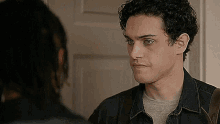 a man with curly hair is standing next to another man in front of a door .