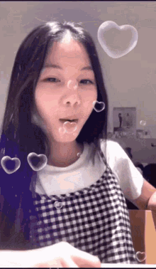 a girl in a plaid dress with heart shaped soap bubbles around her