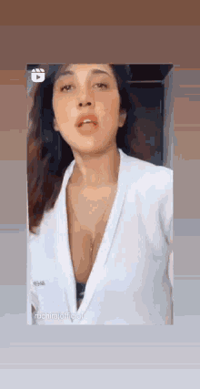 a woman is wearing a white robe with a plunging neckline and a necklace around her neck .