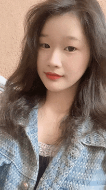 a woman with long dark hair is wearing a denim jacket and red lipstick