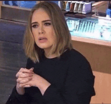 a woman in a black sweater is making a funny face with her hands folded .