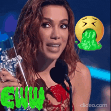 a woman is holding a trophy and talking into a microphone while a green smiley face is vomiting .