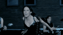 a woman in a black dress is dancing in front of a brick building