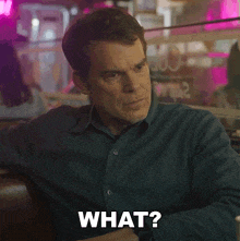 a man in a blue shirt is sitting at a table with the word what on his face