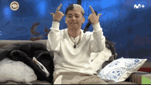 a man sitting on a couch with a m + logo on the bottom right