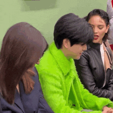 a man in a neon green fur coat sits with two women