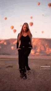 a woman standing in a field with hot air balloons in the background .