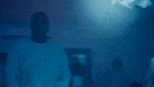 a man is standing in a dark room with his hands on his hips and a woman is sitting on a couch .