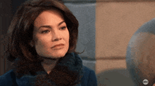 a woman in a blue coat and scarf is looking at the camera with a serious look on her face .