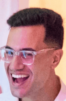 a man wearing glasses is laughing with his mouth open .