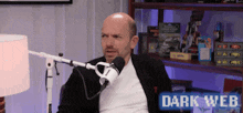 a man is sitting in front of a microphone with the words dark web written on the bottom .