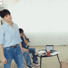 a man in a blue shirt walks past a man sitting in a chair with a laptop on a table