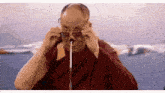 a man in a red robe is adjusting his glasses while speaking into a microphone