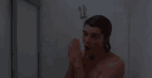 a shirtless man is taking a shower and looking at himself in the mirror
