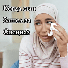 a woman in a hijab wipes her eyes with a napkin in a foreign language