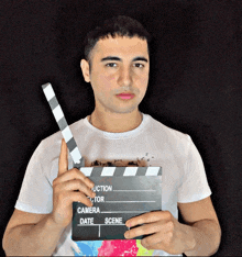 a man in a white shirt is holding a clapper board that says camera date and scene