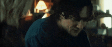 a man in a blue shirt is sitting in a dark room with his eyes closed .
