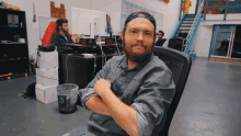 a man with a beard sits at a desk with his arms crossed and a trash can in front of him