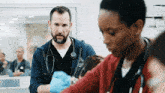 a man with a beard and a stethoscope is talking to a woman in a hospital .