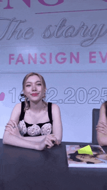 a woman sits at a table in front of a sign that says fansign ev