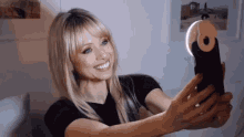 a woman smiles while taking a selfie with a light attached to her phone