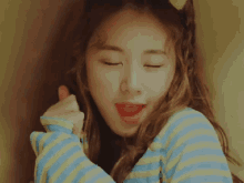 a young woman wearing a blue and yellow striped shirt giving a thumbs up