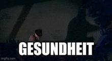 a man in a hat is holding a gun in front of a wall with the word gesundheit on it .