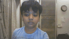 a boy in a blue shirt is standing in front of a clock that says 7:15
