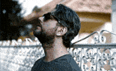 a man with a beard wearing sunglasses is standing in front of a fence .