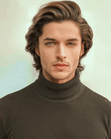 a young man wearing a black turtleneck sweater looks at the camera