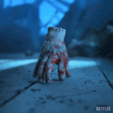 a bloody hand is sitting on a wooden table with a netflix logo in the corner
