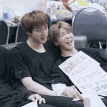 two young men are sitting next to each other with one holding a sign that says ' i love you ' on it