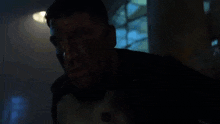 a man with blood on his face is holding a gun in his hand in a dark room .