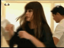 a woman in a black dress is dancing with a man in a white shirt behind her on a tv screen .