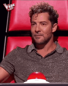 a man with curly hair is sitting in a red chair with the word kids on the back