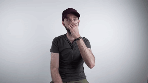 a man wearing a hat and glasses covering his mouth with his hand